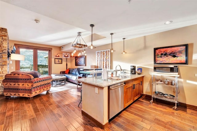 kitchen featuring a peninsula, stainless steel dishwasher, a kitchen breakfast bar, a sink, and wood finished floors