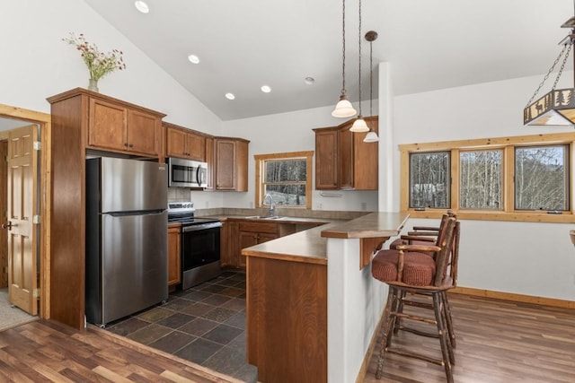 32596 Ute Trl, Oak Creek, CO 80467 - kitchen featuring appliances with stainless steel finishes, a peninsula, vaulted ceiling, brown cabinetry, and a breakfast bar