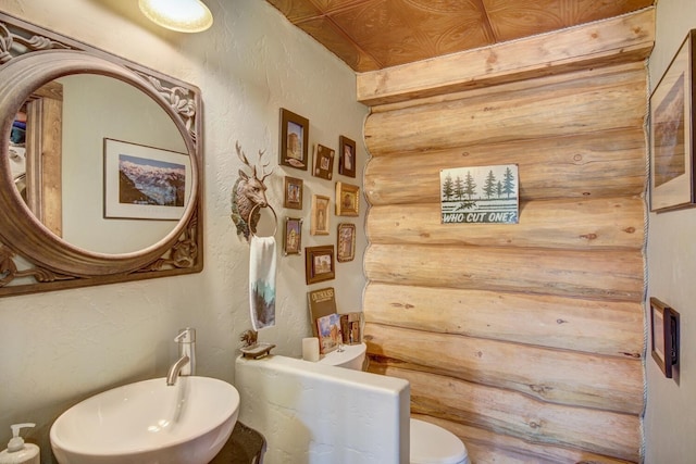 half bath featuring toilet, a textured wall, and a sink