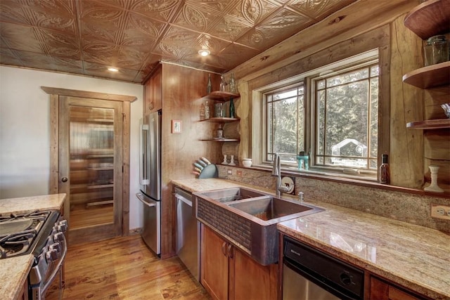 kitchen featuring open shelves, a sink, brown cabinets, light wood-type flooring, and appliances with stainless steel finishes