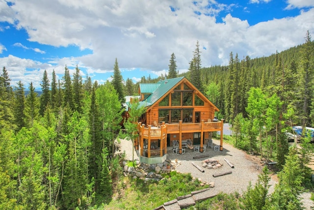 rear view of house with log exterior, a wooden deck, a wooded view, a patio, and metal roof