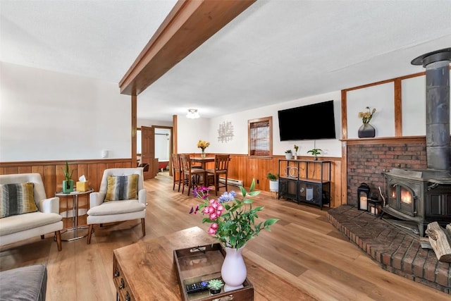 211 W Oak St, Oak Creek, CO 80467 - living area with a wood stove, wainscoting, wood finished floors, beamed ceiling, and a baseboard heating unit