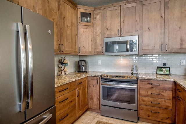 131 Allegra Ln Unit 131, Silverthorne, CO 80498 - kitchen with appliances with stainless steel finishes, backsplash, brown cabinets, light tile patterned floors, and light stone counters