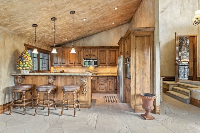 165 River Park Dr, Breckenridge, CO 80424 - kitchen with appliances with stainless steel finishes, stone tile floors, brown cabinetry, a breakfast bar, and a peninsula