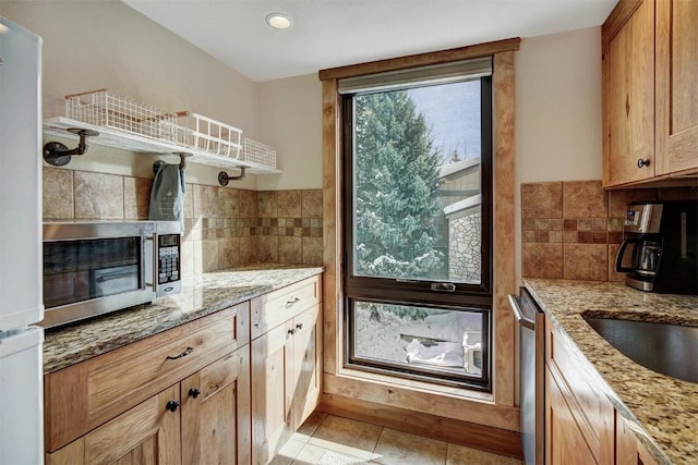 kitchen with tasteful backsplash, light stone countertops, appliances with stainless steel finishes, and light tile patterned floors