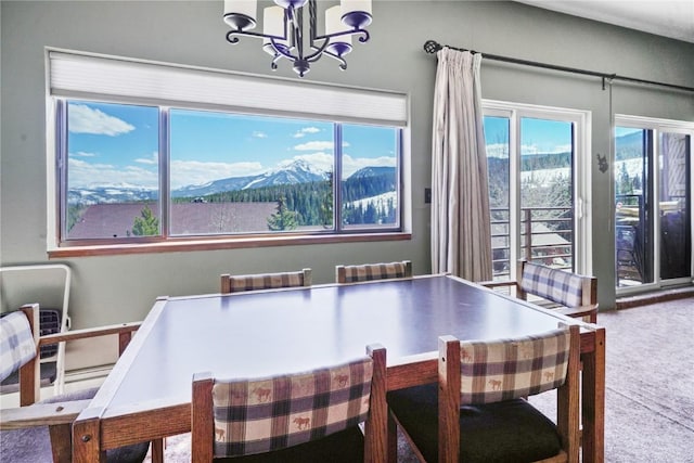 carpeted dining space featuring radiator heating unit, a healthy amount of sunlight, a notable chandelier, and a mountain view