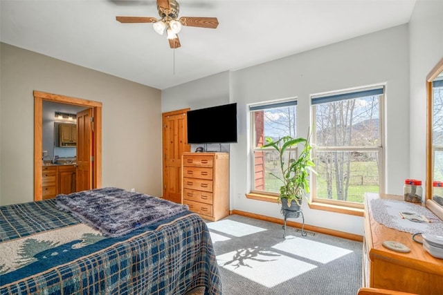 carpeted bedroom with a ceiling fan, baseboards, and ensuite bath