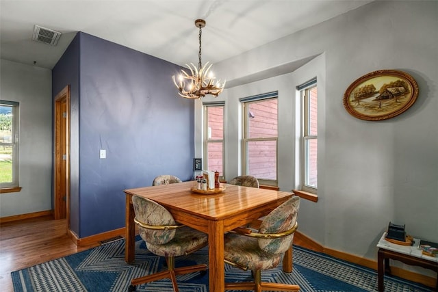 dining space with baseboards, an inviting chandelier, wood finished floors, and visible vents