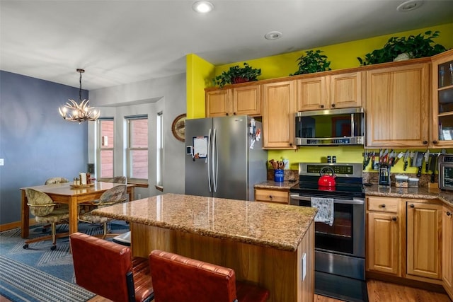 kitchen featuring a notable chandelier, light stone counters, stainless steel appliances, a kitchen bar, and a kitchen island