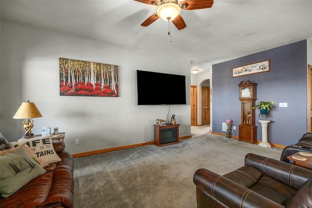 living area featuring arched walkways, a ceiling fan, baseboards, and carpet