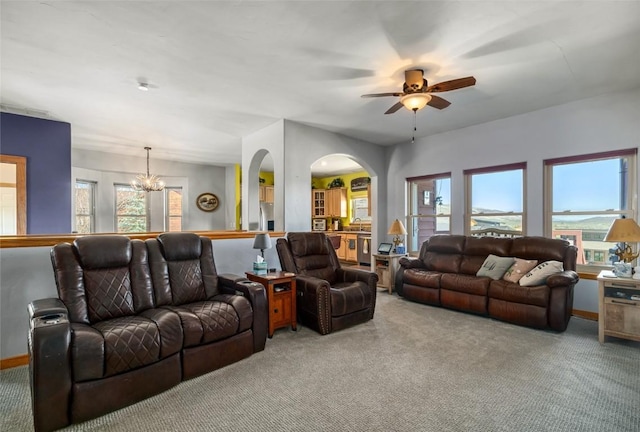 living area with baseboards, arched walkways, ceiling fan with notable chandelier, and light carpet