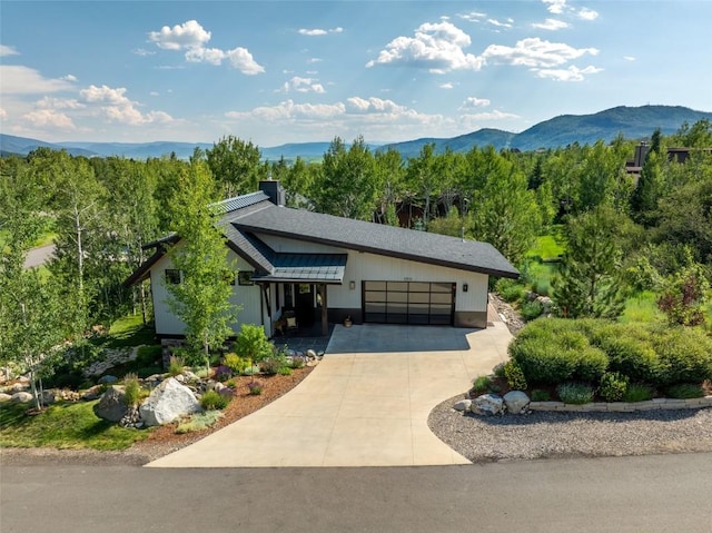 1511 Harwig Cir, Steamboat Springs, CO 80487 - view of front facade with an attached garage, a view of trees, a mountain view, a chimney, and driveway