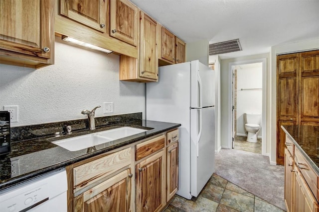 kitchen featuring dark stone countertops, visible vents, a sink, and white appliances