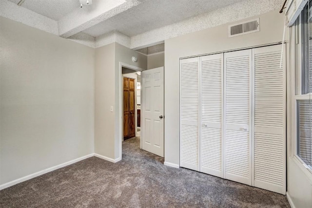 unfurnished bedroom with carpet flooring, a closet, a textured ceiling, visible vents, and baseboards