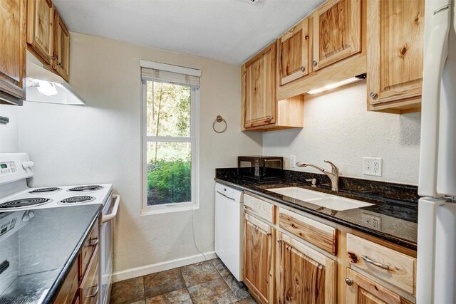 kitchen with under cabinet range hood, baseboards, white appliances, stone finish flooring, and a sink