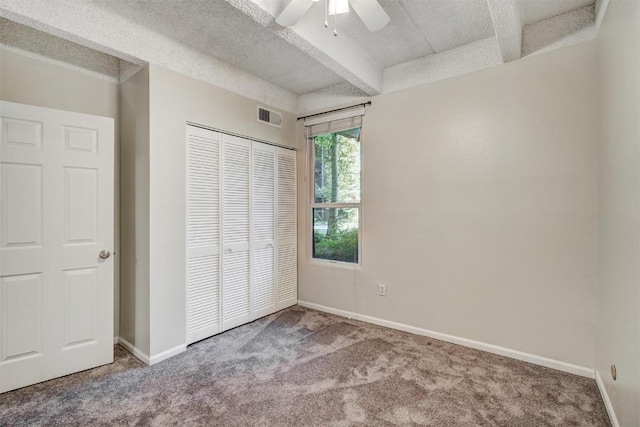unfurnished bedroom featuring a closet, baseboards, beamed ceiling, and carpet floors