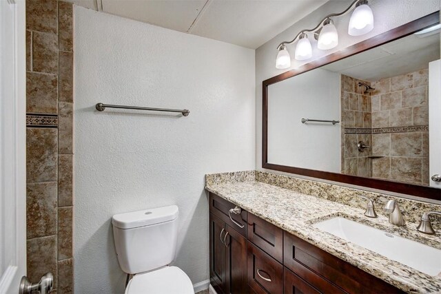 bathroom featuring toilet, tiled shower, and vanity