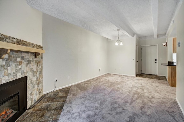 unfurnished living room with a notable chandelier, a textured ceiling, baseboards, a stone fireplace, and dark carpet