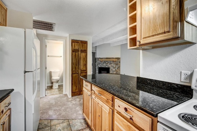 kitchen featuring freestanding refrigerator, a stone fireplace, electric range oven, visible vents, and dark stone countertops