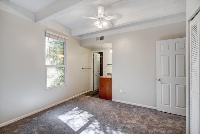 unfurnished bedroom with beam ceiling, dark carpet, ensuite bathroom, visible vents, and baseboards