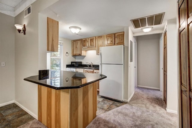 kitchen featuring freestanding refrigerator, a peninsula, visible vents, and a sink