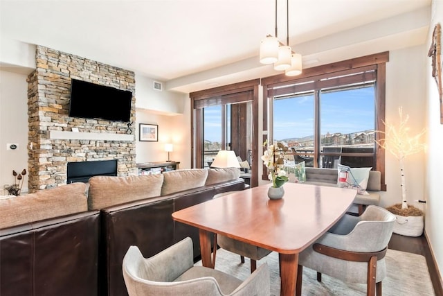 dining room featuring wood finished floors, visible vents, and a stone fireplace