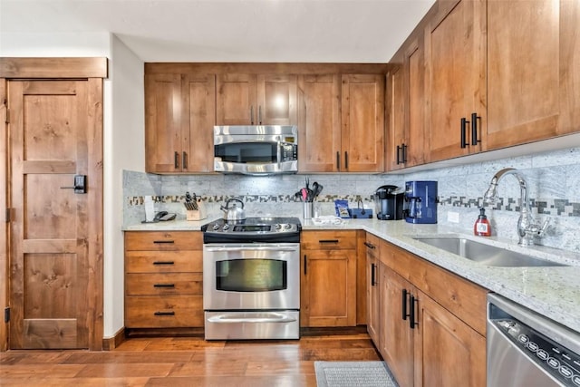 kitchen with wood finished floors, brown cabinetry, a sink, tasteful backsplash, and appliances with stainless steel finishes
