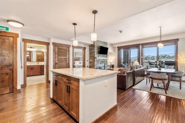 kitchen featuring light stone counters, a kitchen island, hardwood / wood-style floors, a fireplace, and hanging light fixtures