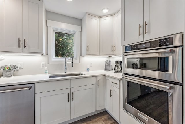 kitchen with hardwood / wood-style floors, appliances with stainless steel finishes, white cabinetry, and sink