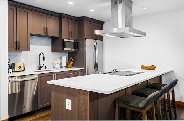 kitchen with stainless steel appliances, a breakfast bar, backsplash, island range hood, and a sink