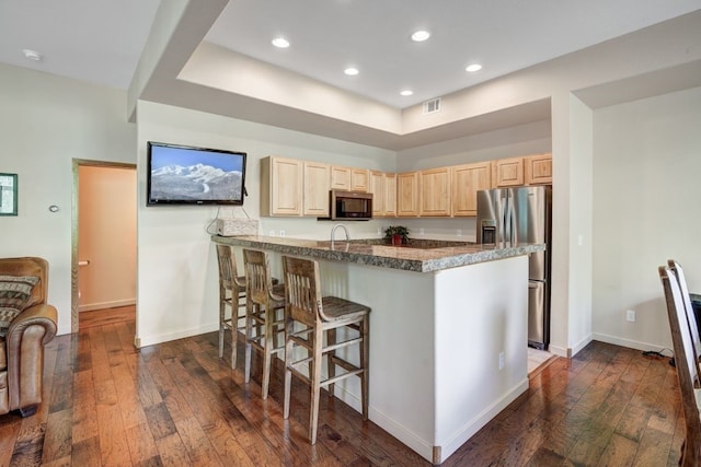 180 Robin Dr Unit 180, Silverthorne, CO 80498 - kitchen with appliances with stainless steel finishes, light brown cabinetry, dark wood-style floors, a kitchen breakfast bar, and a peninsula