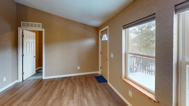 foyer entrance with lofted ceiling, visible vents, wood finished floors, and a textured wall