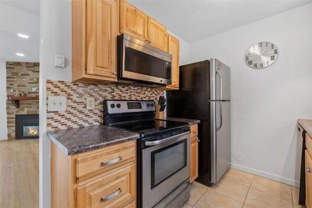 1565 Shadow Run Frontage Unit 103, Steamboat Springs, CO 80487 - kitchen featuring appliances with stainless steel finishes, dark countertops, tasteful backsplash, a stone fireplace, and baseboards