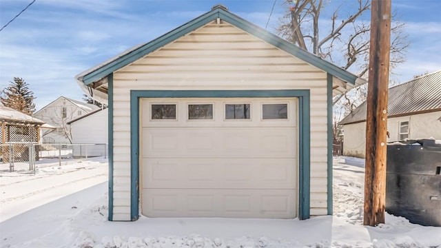 snow covered garage with fence and a detached garage