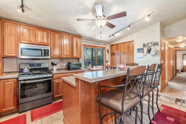 27125 Moonlight Way, Steamboat Springs, CO 80487 - kitchen with stainless steel appliances, rail lighting, lofted ceiling, a breakfast bar, and a center island