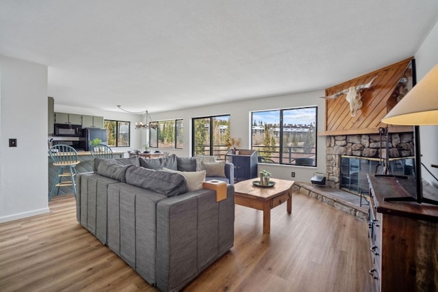 9876 Ryan Gulch Rd Unit 206, Silverthorne, CO 80498 - living room featuring light wood-style flooring, a chandelier, baseboards, and a stone fireplace