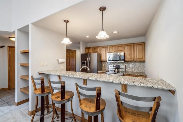 kitchen featuring light stone counters, tasteful backsplash, hanging light fixtures, stainless steel appliances, and a peninsula
