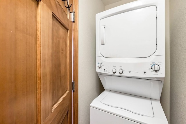 laundry area with a textured wall, stacked washer / drying machine, and laundry area