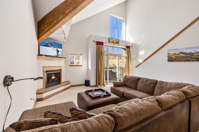 living room featuring a glass covered fireplace, baseboards, carpet flooring, and high vaulted ceiling
