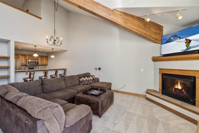 living area featuring a glass covered fireplace, light colored carpet, rail lighting, baseboards, and a notable chandelier