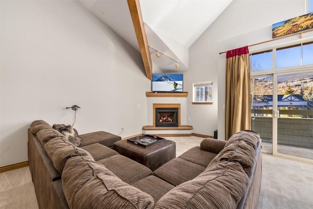 living room featuring high vaulted ceiling, a warm lit fireplace, light colored carpet, and baseboards