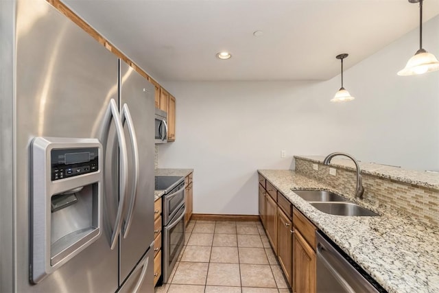 kitchen with a sink, brown cabinetry, stainless steel appliances, decorative light fixtures, and baseboards