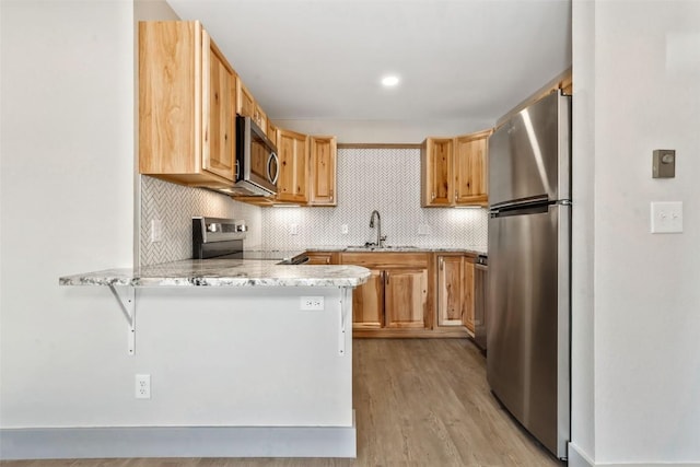 kitchen featuring stainless steel appliances, a sink, light wood-style floors, a peninsula, and tasteful backsplash