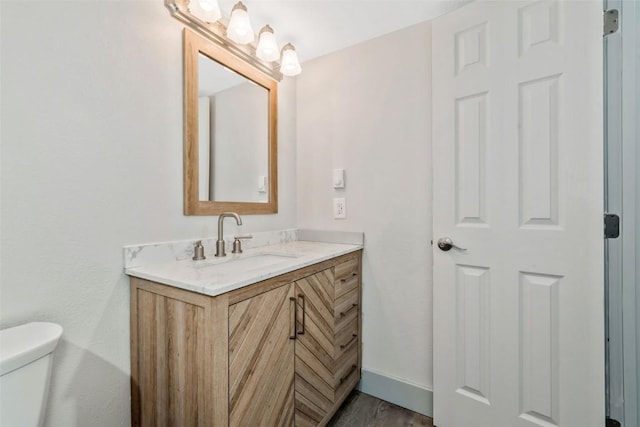 half bath featuring toilet, vanity, wood finished floors, and baseboards