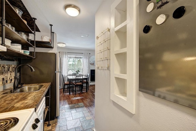 kitchen featuring open shelves, a sink, range, stone finish flooring, and backsplash