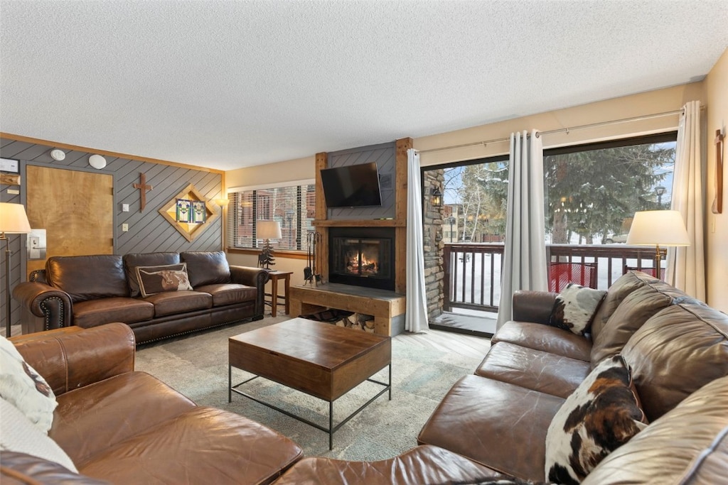 carpeted living room with a textured ceiling, a large fireplace, and wood walls