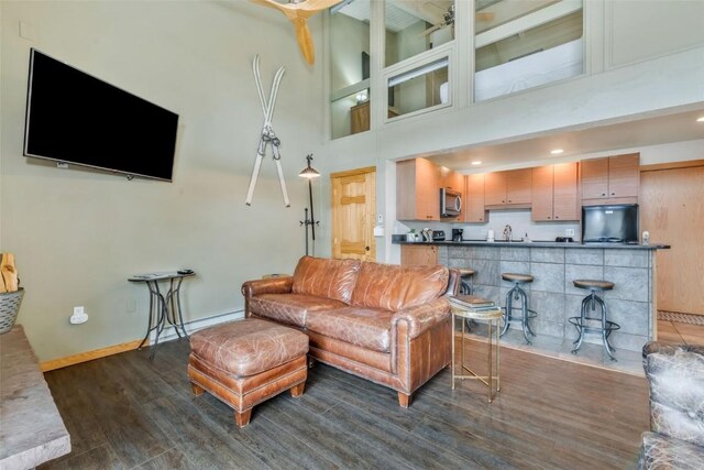 living room with dark wood-type flooring, a towering ceiling, and baseboards