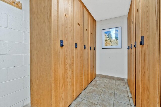 hall featuring light tile patterned flooring and concrete block wall