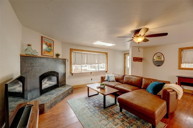 living area with a tiled fireplace, baseboards, ceiling fan, and wood finished floors