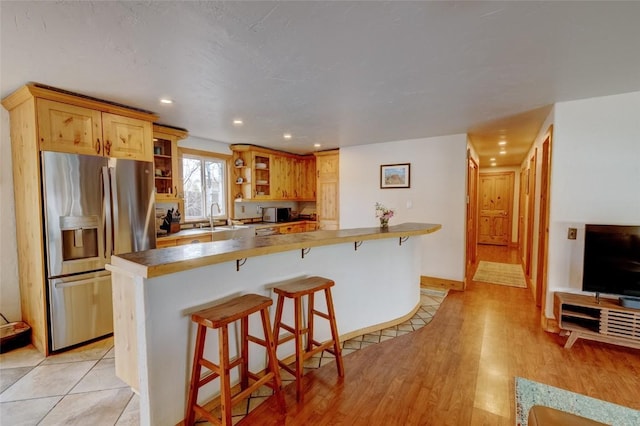 kitchen with stainless steel fridge, glass insert cabinets, recessed lighting, and a kitchen bar